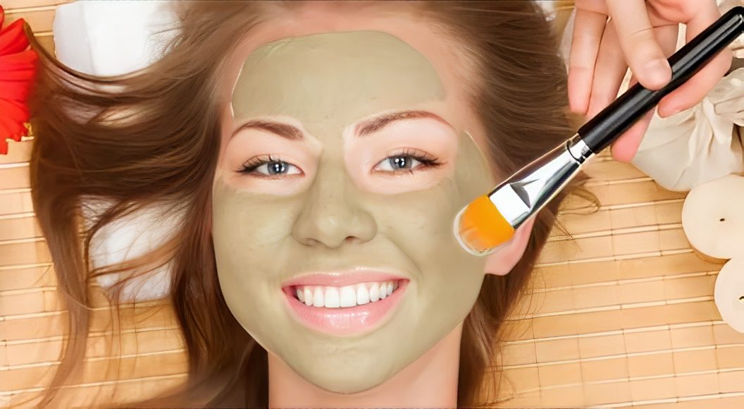 Smiling woman with green facial mask applied.