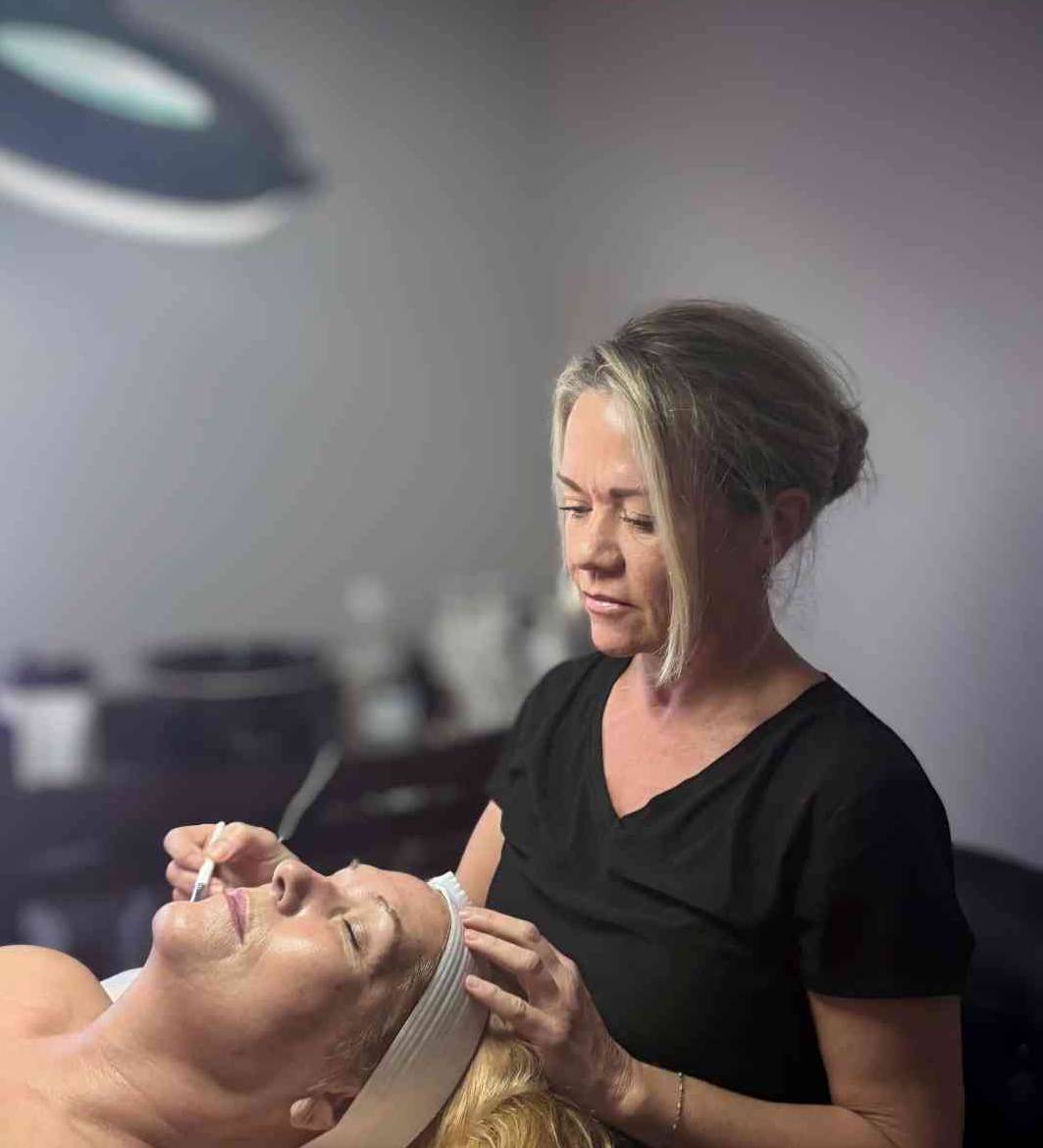 A woman carefully applies skincare treatment to a client's face.