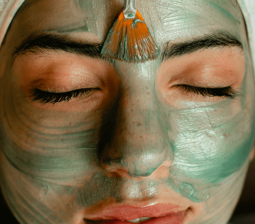 Close-up of a person with a green facial mask and eyes closed.
