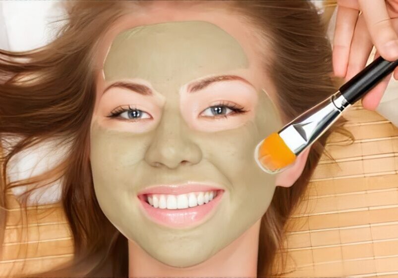 Smiling woman with green facial mask applied.